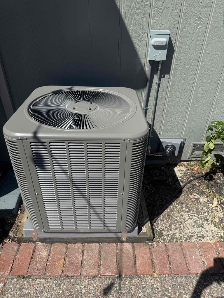 Traditional top-discharge AC condenser installed on a pad beside a San Rafael home with electrical disconnect